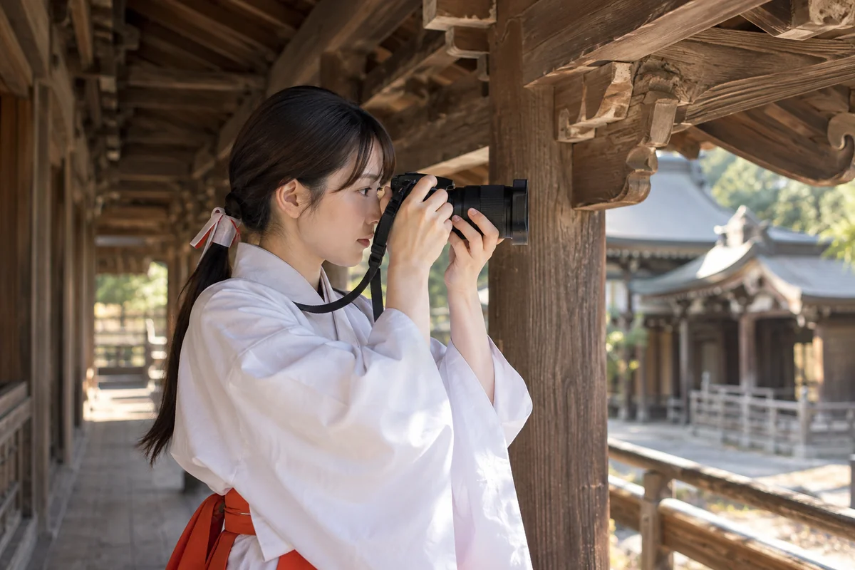 カメラを両手で構え、木造建築の細部を記録する巫女装束の人物